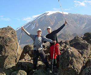 Drs. Shockey standing on rocky terrain with climbing poles smiling with Mount Kilimanjaro in the backgound.
